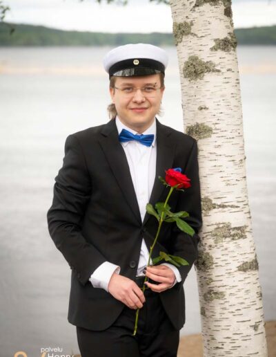 Ylioppilas poseeraa kukka koivuun nojaten.