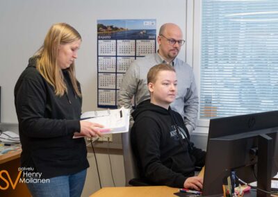 Kaksi miestä ja nainen katsoo dokumentteja päätteen ääressä.