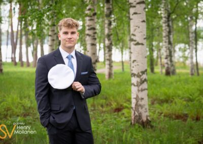Ylioppilas poseeraa kameralle koivikossa.