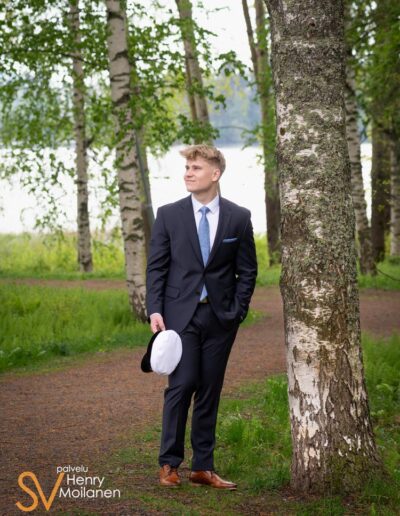 Ylioppilas seisoo puun vieressä.