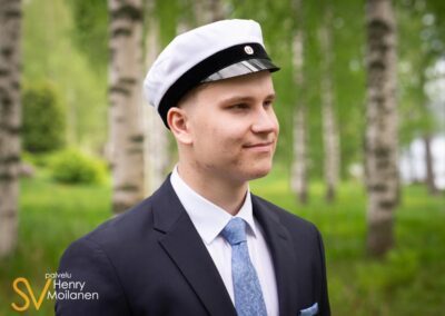 Ylioppilas katsoo vasemmalle koivikossa.