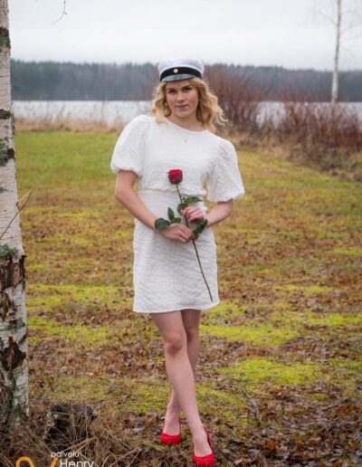 Ylioppilas seisoo syksyisellä nurmikolla ruusu kädessä.