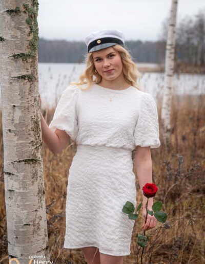 Ylioppilas seisoo koivikossa ruusu kädessä.