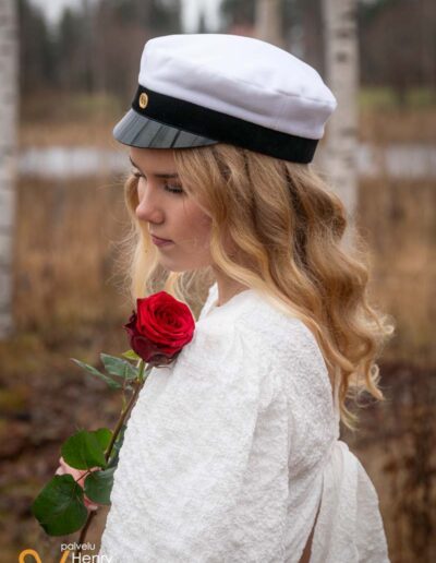 Ylioppilas seisoo koivikossa ruusu kädessä.