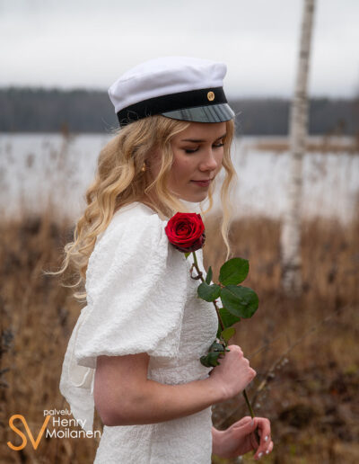 Ylioppilas seisoo rannan läheisyydessä ruusu kädessä.