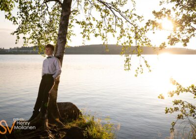 Poika nojaa koivuun rannalla.