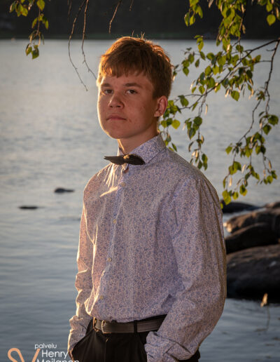 Poika seisoo rannalla kädet taskuissa.