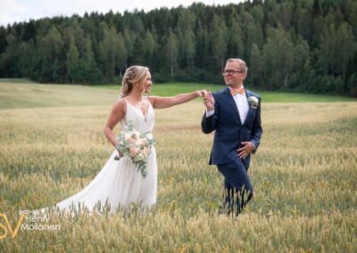 Hääpari kävelee käsi kädessä viljapellolla.