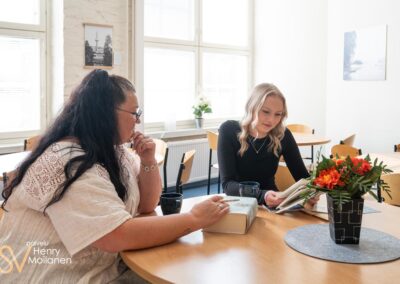 Nainen lukee kirjaa, toinen nainen istuu vieressä.