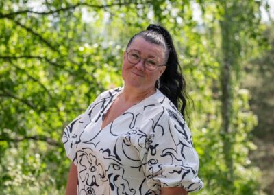 Nainen seisoo puistossa toinen käsi taskussa.