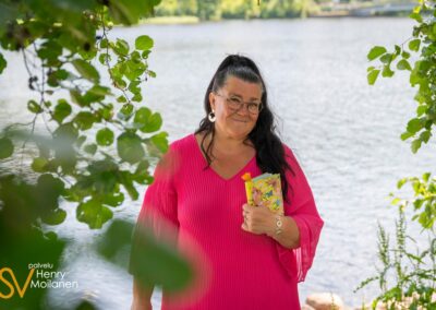 Nainen seisoo rannalla kirja kädessä.