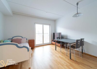 Avara huone, sänky vasemmalla ja keittiön pöytä oikealla.