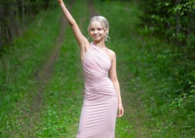 Tyttö nostaa ylioppilaslakkia metsäautotiellä.